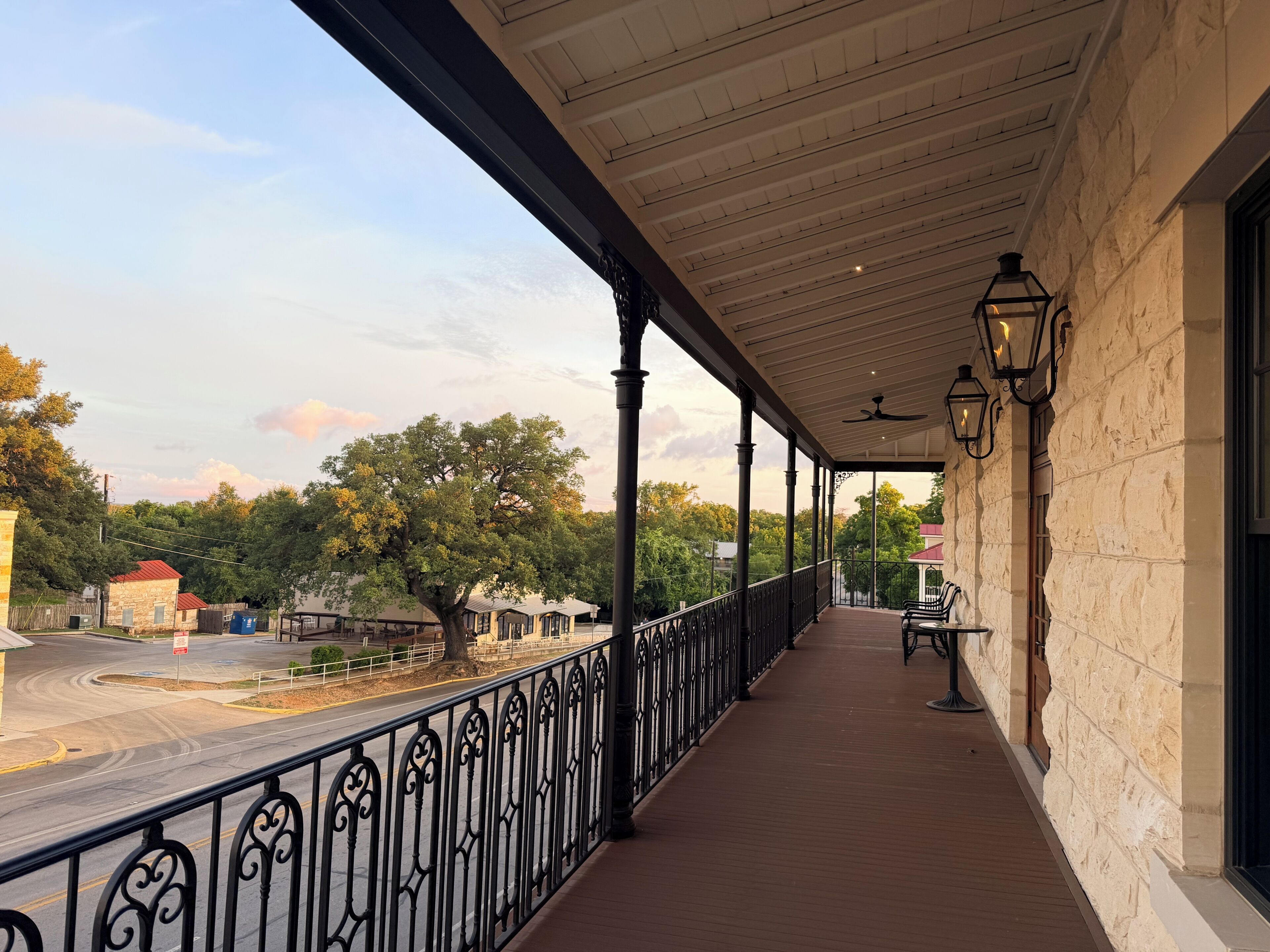 A covered balcony with a railing, stone wall, and a view of the street and trees.