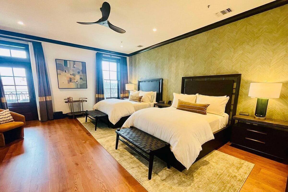 A hotel room with two beds, a ceiling fan, a TV, and a desk with a lamp.