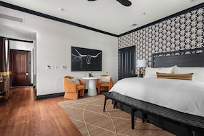A hotel room with a bed, a desk, two chairs, a wall-mounted artwork, and a patterned wallpaper.
