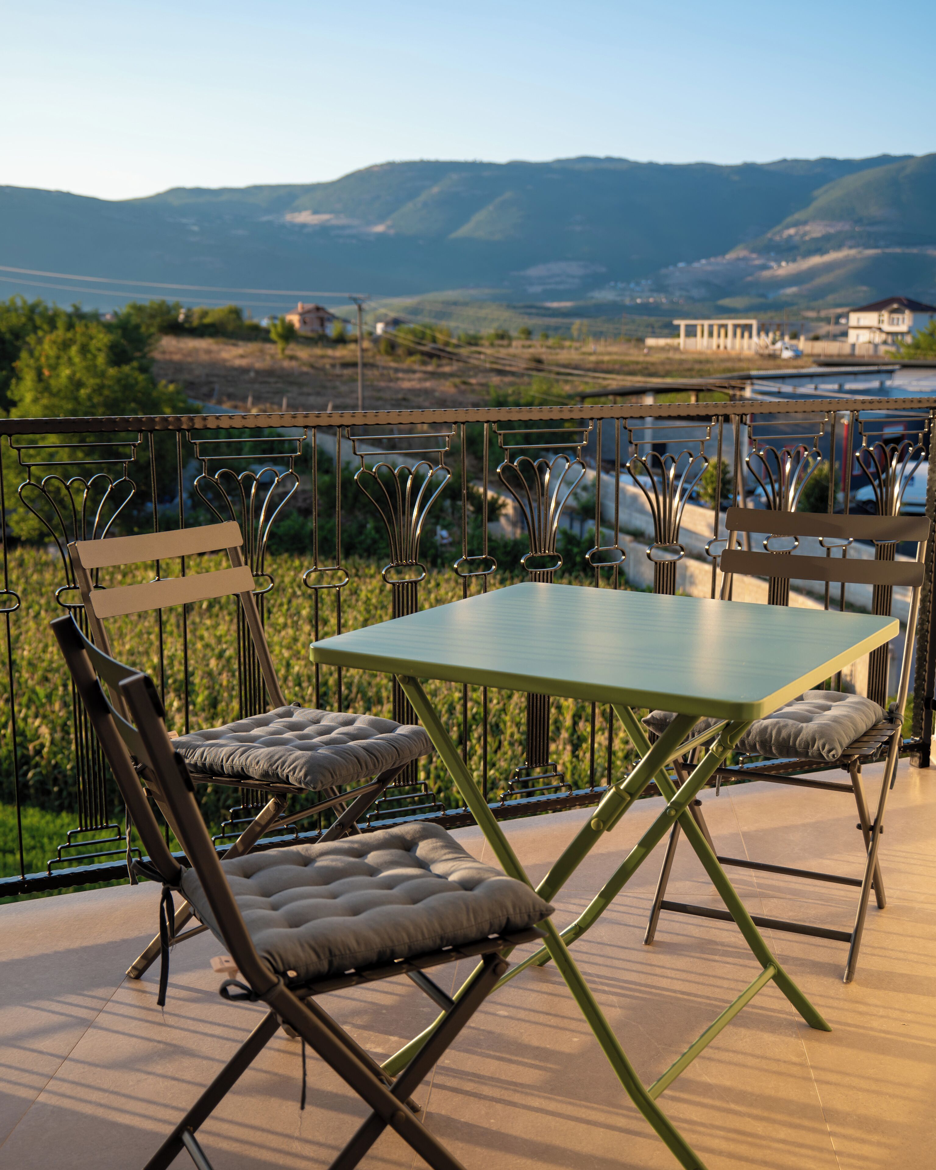 A terrace with a table and chairs, overlooking a scenic landscape with hills and a building in the distance.