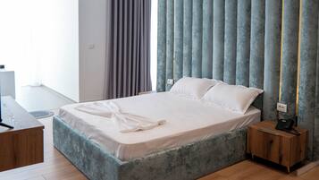 A modern bedroom with a large bed, wooden flooring, and a bedside table with a lamp.
