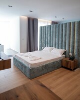 A modern bedroom with a large bed, wooden flooring, and a bedside table with a lamp.