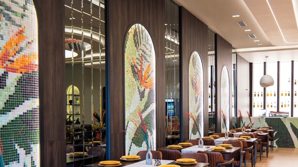 A modern restaurant interior with long tables, leather chairs, and mosaic art on the walls. - Leo Hotel (Shtiqën)