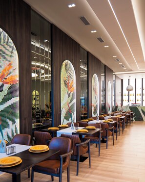 A modern restaurant interior with long tables, leather chairs, and mosaic art on the walls. - Leo Hotel (Shtiqën)