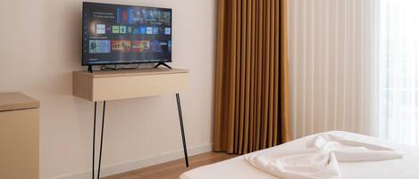 A hotel room with a bed, a TV on a stand, a nightstand, and a window with curtains.