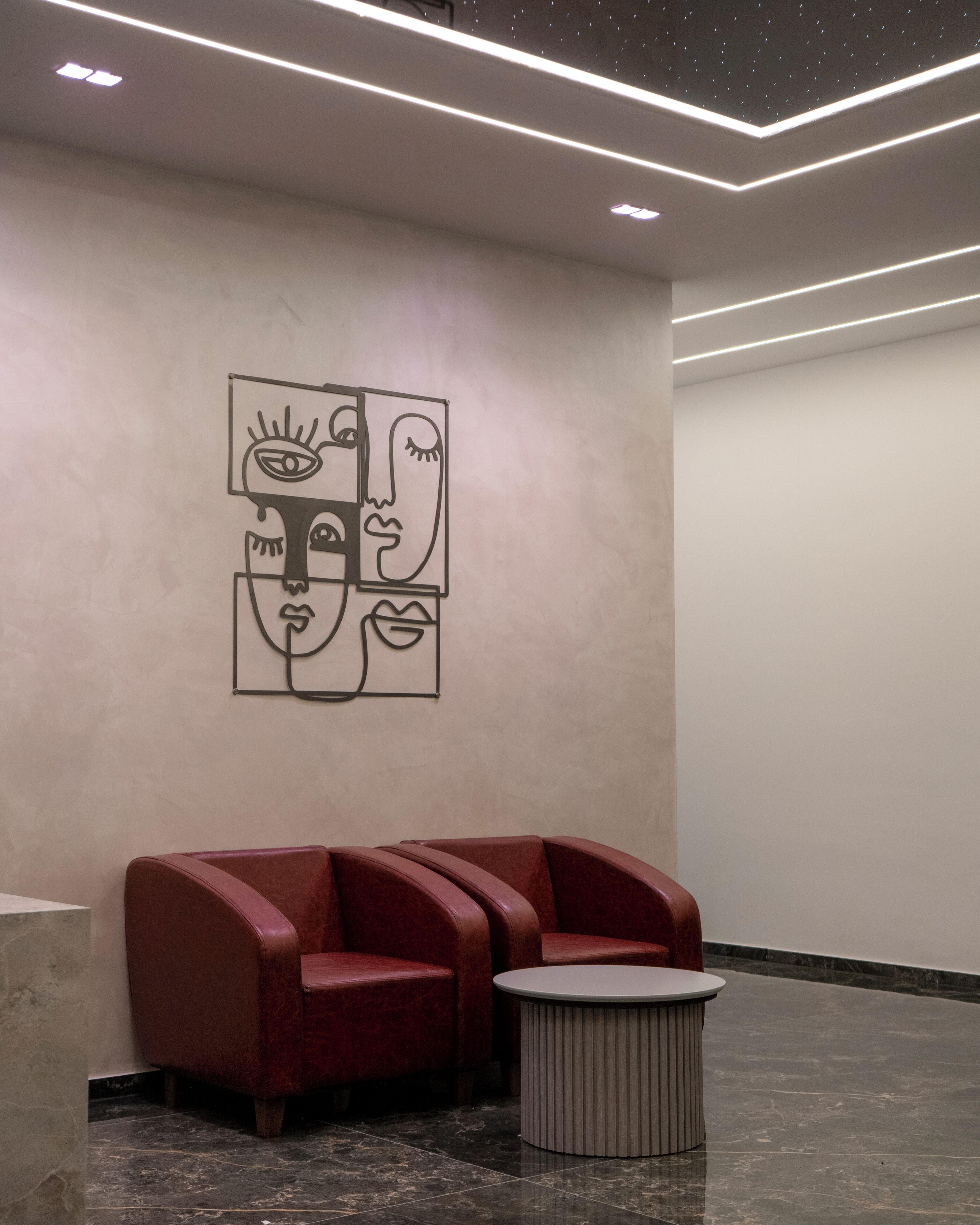 A waiting area with a modern design, featuring a geometric wall art, red seating, and a small round table.