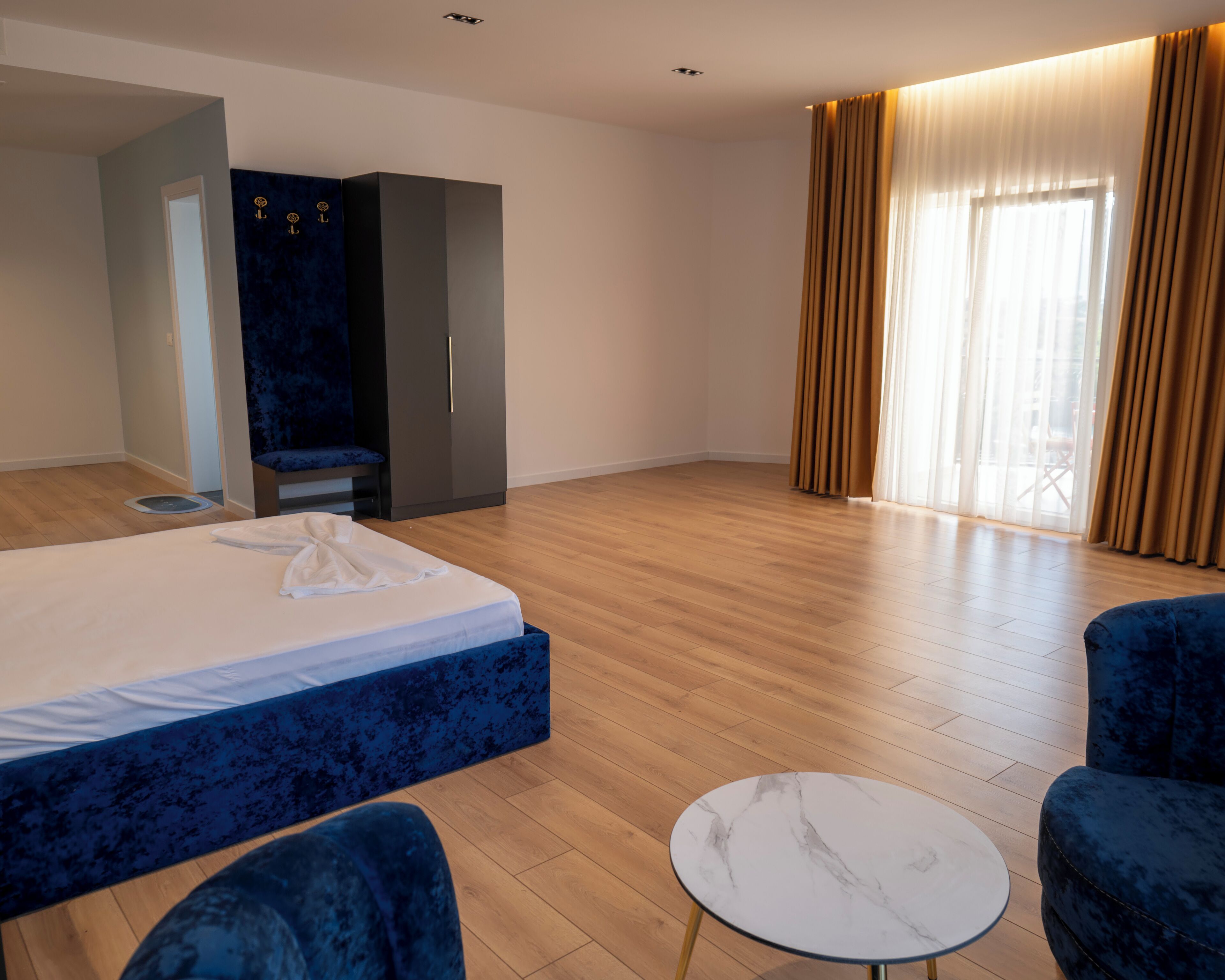 Una habitación de hotel con cama, dos sillones, una mesita redonda, armario y un ventanal con cortinas.