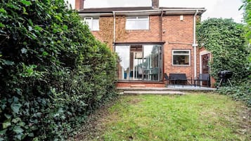 A two-story brick house with a glass door entrance, a patio with outdoor seating, and a barbecue grill.