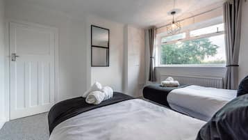 A hotel room with two beds, a window with curtains, a radiator, and a door.