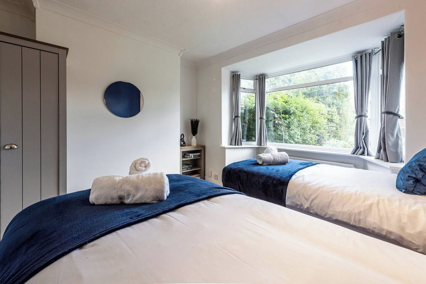 Ein Schlafzimmer mit zwei Betten, einem Kleiderschrank, einem Fenster mit Vorhängen und einem runden Gegenstand an der Wand.