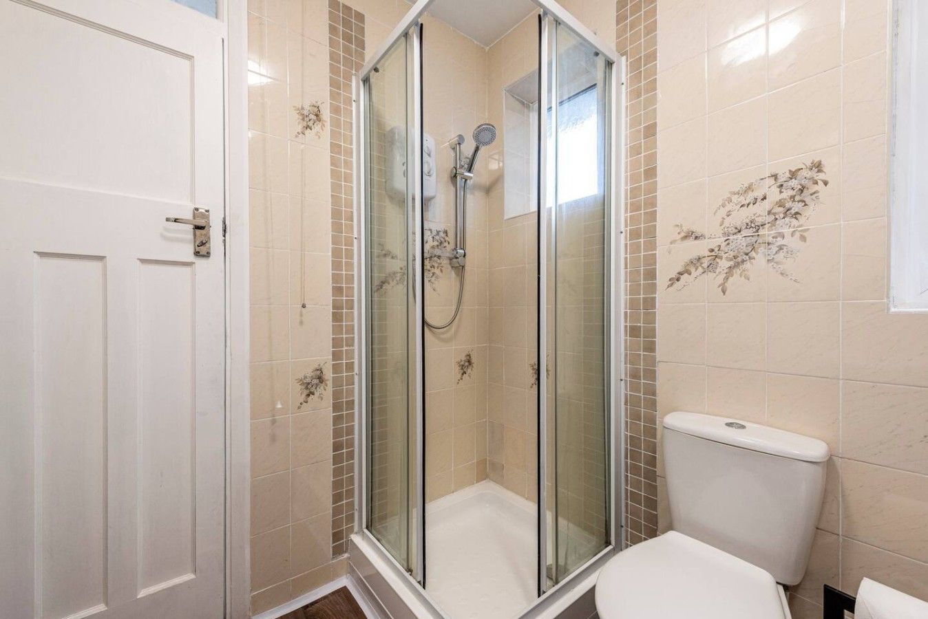 A bathroom with a glass-enclosed shower, a toilet, and a door.