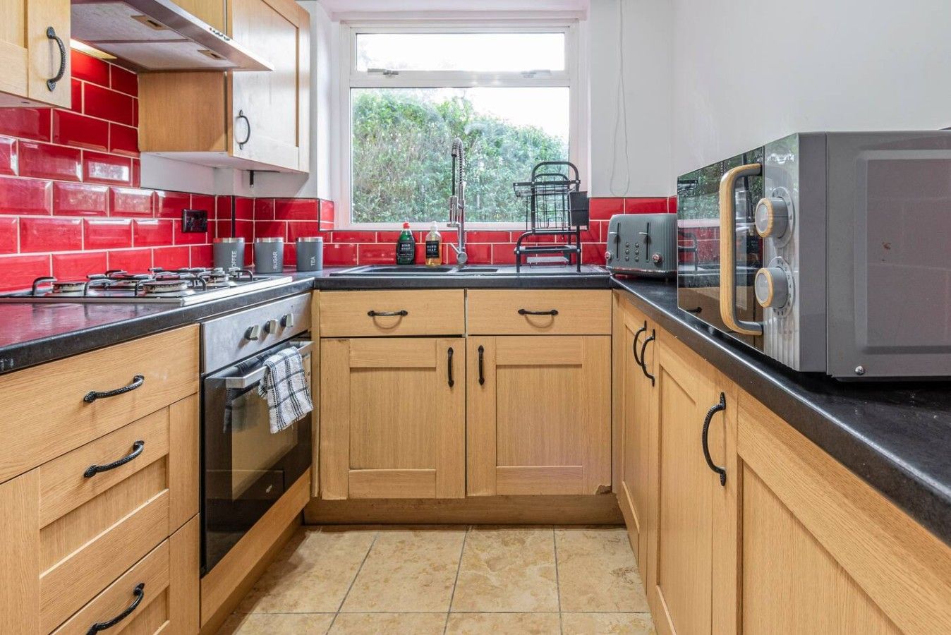 A kitchen with wooden cabinets, a gas stove, a microwave, and a window with a view of greenery.