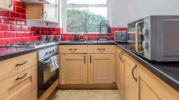 A kitchen with wooden cabinets, a gas stove, a microwave, and a window with a view of greenery.