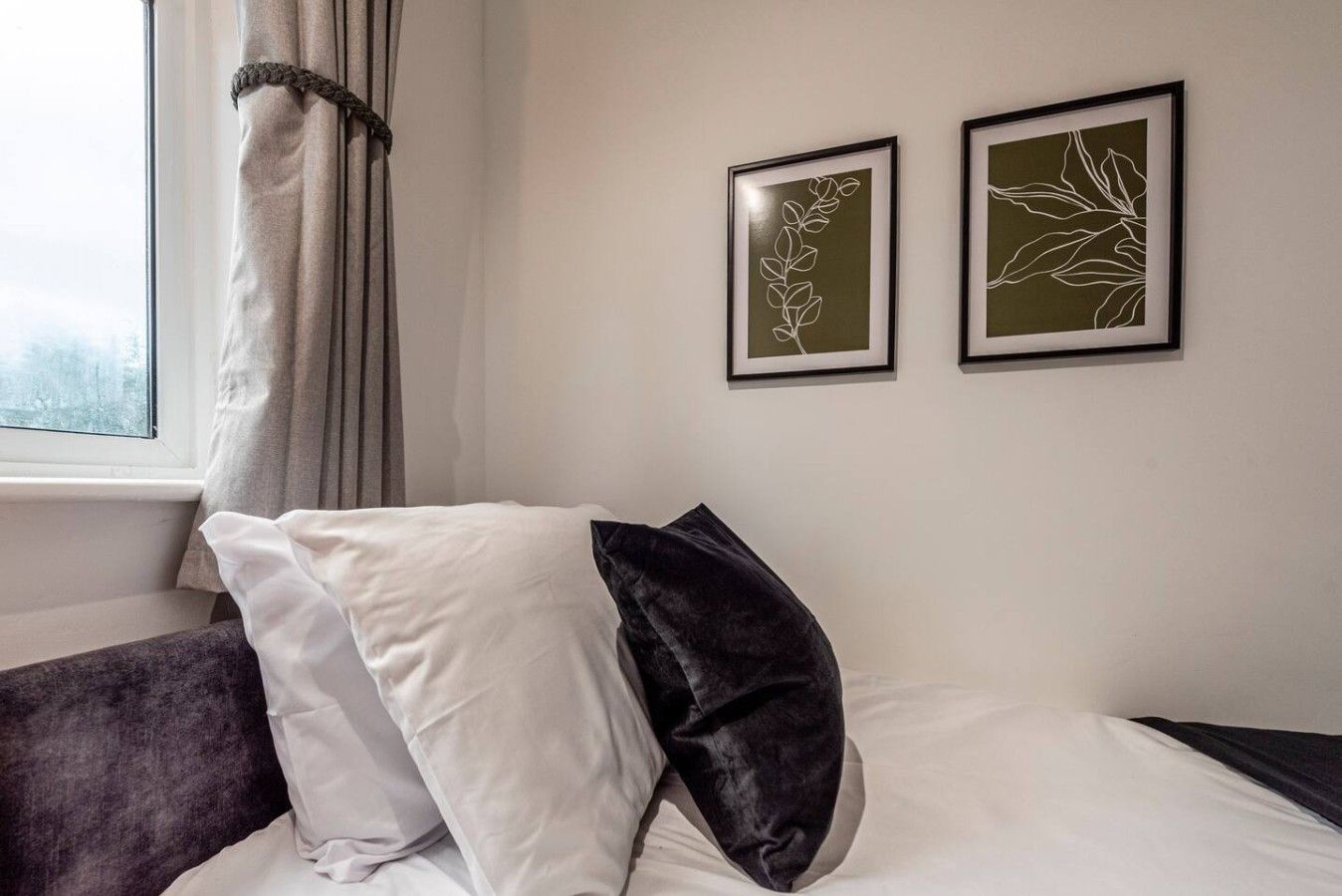 Une chambre d’hôtel avec un lit, deux œuvres d’art encadrées accrochées au mur, une fenêtre avec des rideaux et une vue sur l’extérieur.