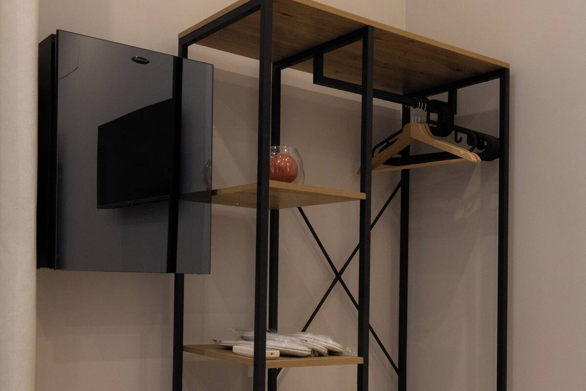 A corner wardrobe with a TV mounted on the wall, wooden shelves, and a lower cabinet with drawers.