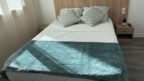 A neatly made bed with patterned pillows, a wooden headboard, and a bedside table with a remote control and a small plant. - Central Hotel (Saint-Priest)