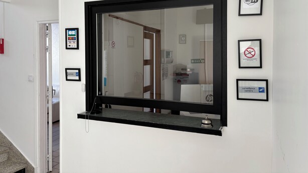 A reception area with a large window, a reception desk, and several framed signs including Wi-Fi, no smoking, and surveillance camera. - Central Hotel (Saint-Priest)