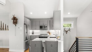 Une cuisine moderne avec des meubles blancs, des appareils en acier inoxydable et un îlot central doté de deux tabourets.