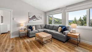 Un salon moderne avec un canapé d’angle, deux tables basses en bois et une grande fenêtre offrant une vue panoramique.
