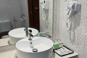 Ein Badezimmer mit rundem Waschbecken, einem Spiegel, einem Föhn und einem Telefon.