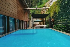 A swimming pool with a wooden deck, a covered seating area, and a green wall with plants. - Lereng Bromo Hotel (Tosari)