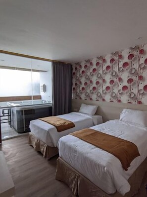 Habitación de hotel con dos camas, un escritorio y vistas al exterior.
