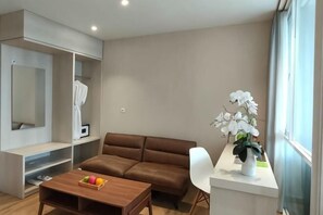 A modern living room with a brown sofa, a wooden coffee table, a white chair, a white vase with flowers, and a built-in shelving unit. - Lereng Bromo Hotel (Tosari)