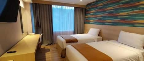 A hotel room with two beds, a desk, a TV, and a large window with curtains.