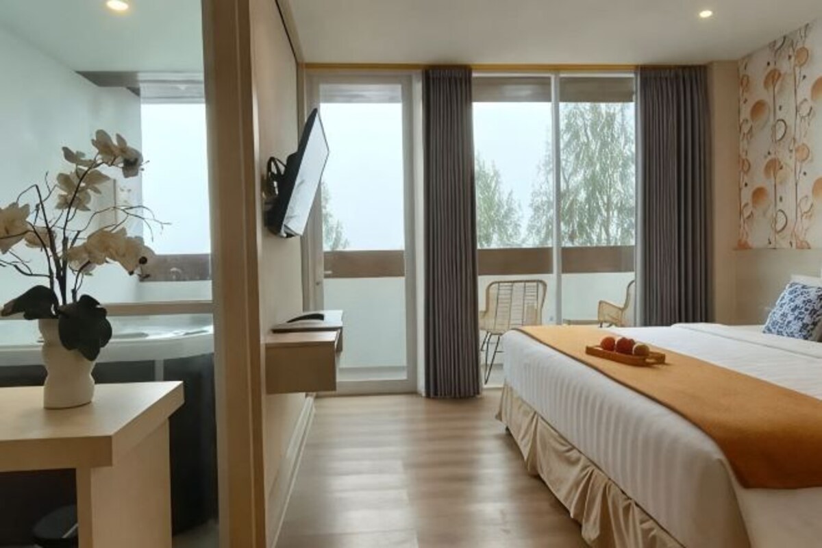 A hotel room with a bed, a desk, a chair, a TV, and a window with curtains.