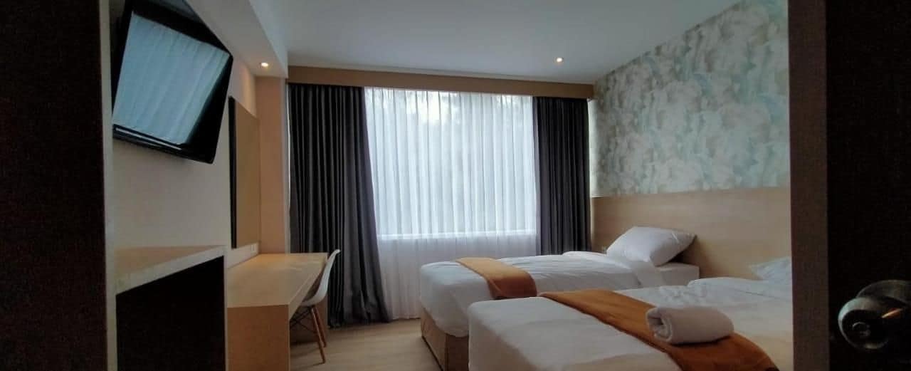 A hotel room with two beds, a desk, and a television.