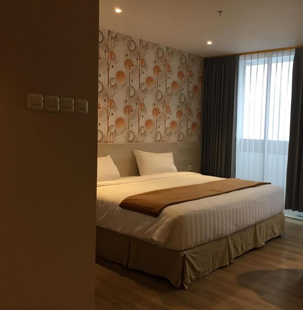 A hotel room with a large bed, a wall with a circular pattern, and a window with curtains.