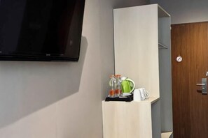 A room with a flat-screen TV mounted on the wall, a wooden cabinet with a kettle and bottles, and a door with a round handle. - Lereng Bromo Hotel (Tosari)