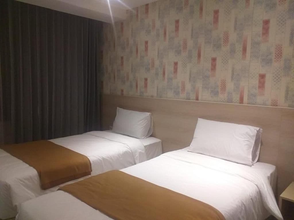 A hotel room with two beds, a patterned wall, and a curtain.