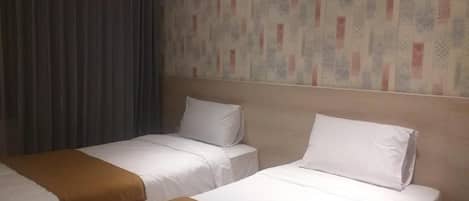 A hotel room with two beds, a patterned wall, and a curtain.