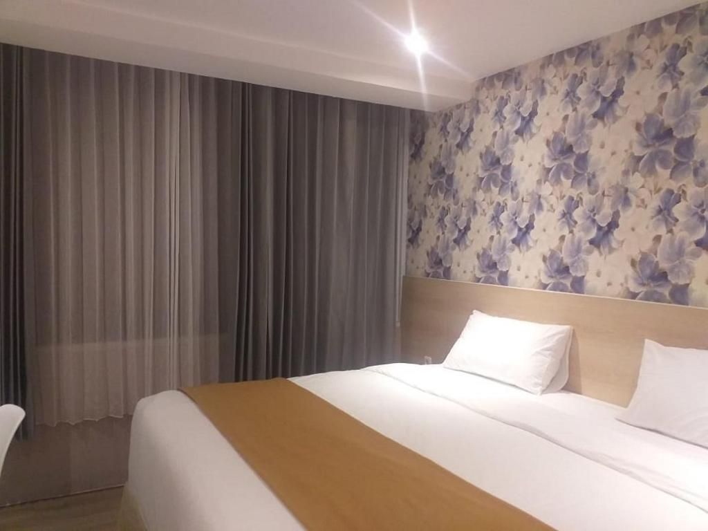 A hotel room with a bed, curtains, and a floral wallpaper.