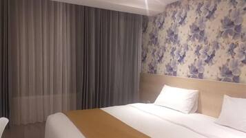 A hotel room with a bed, curtains, and a floral wallpaper.