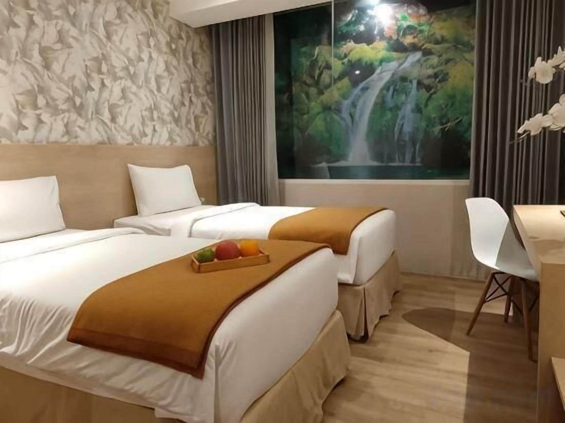 Een hotelkamer met twee bedden, een bureau en een groot raam met uitzicht op een waterval.