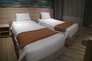 Dos camas individuales con sábanas blancas y mantas marrones, un cabecero de madera y un cuadro en la pared.