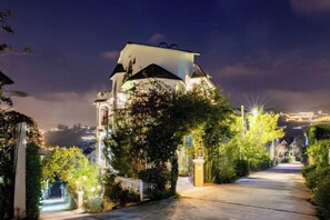 A well-lit pathway leading to a building with a distinct architectural style, surrounded by greenery. - Adalia Villa With ValeyView - O'TEL (Dalat)