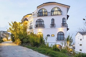 Monikerroksinen rakennus, jossa on parvekkeita, suuret ikkunat ja kulkutie, joka johtaa sisäänkäynnille.