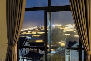 A view through a window with curtains, featuring a cityscape at night. - Adalia Villa With ValeyView - O'TEL (Dalat)