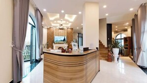 A modern reception area with a curved wooden counter, a television, and a fireplace. - Adalia Villa With ValeyView - O'TEL (Dalat)