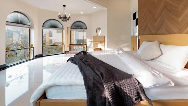 A modern hotel room with a large bed, a chandelier, and large windows with city views. - Adalia Villa With ValeyView - O'TEL (Dalat)