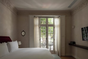 A hotel room with a bed, a mirror, a window with curtains, and a wall-mounted TV. - El Cortés, Member of Relais & Châteaux (Mexico City)