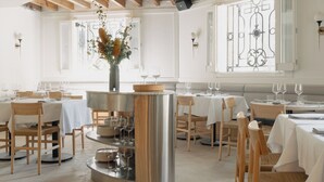 A restaurant interior with wooden beams, white walls, and a central island with a vase of flowers. - El Cortés, Member of Relais & Châteaux (Mexico City)