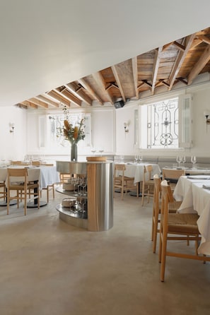 A restaurant interior with wooden beams, white walls, and a central island with a vase of flowers. - El Cortés, Member of Relais & Châteaux (Mexico City)