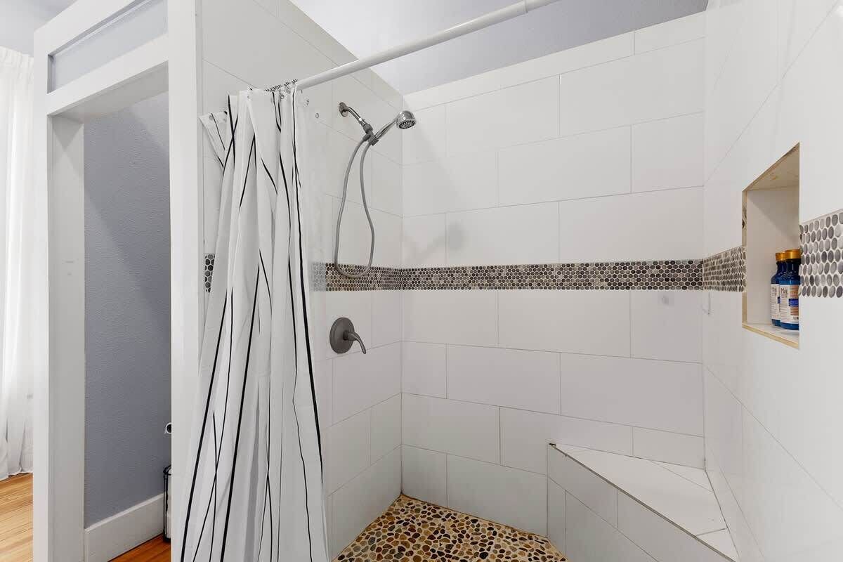 A shower with a tiled wall, a shower curtain, and a shelf with toiletries.