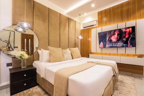 A modern bedroom with a large bed, a TV mounted on the wall, and a bedside table with a vase of flowers.