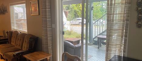 Una sala de estar acogedora con un sofá, una mesa de madera y una silla. Hay un ventanal corredizo que da a un patio al aire libre.