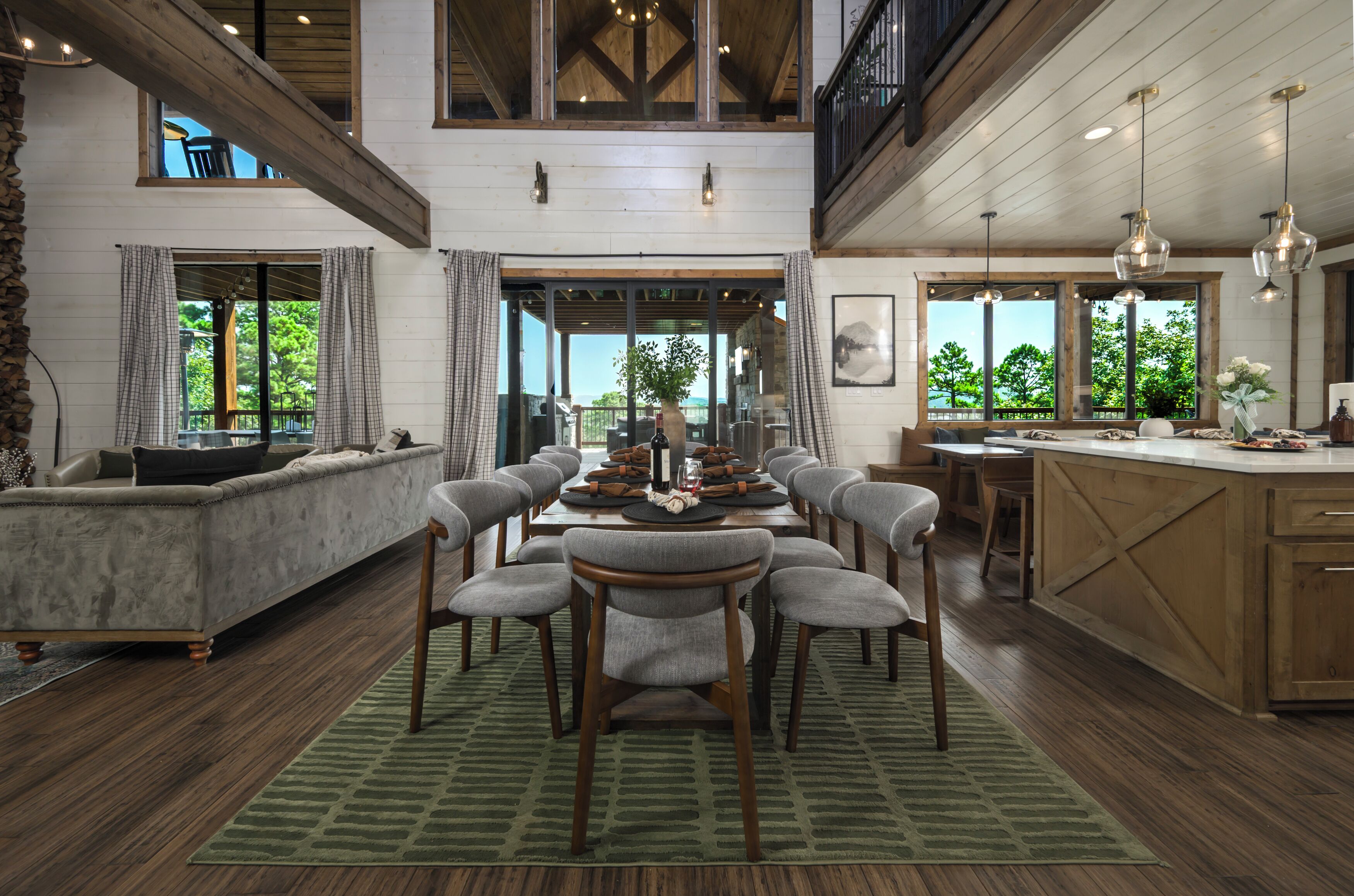 A spacious dining area with a high ceiling and natural light, featuring a long table with chairs and a view of the outdoors.